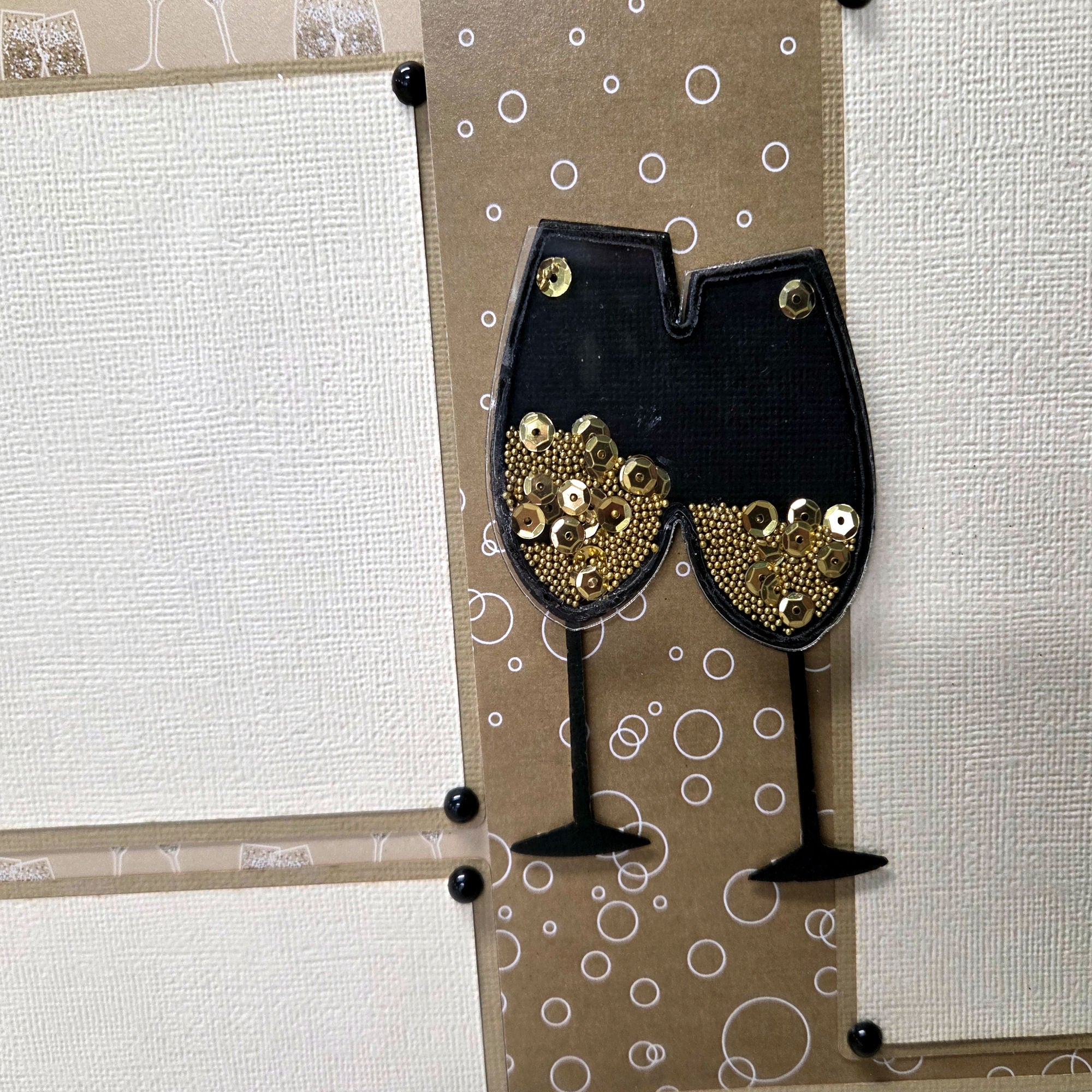 Decorative card with black wine glass cutouts with gold sequins on a patterned background.